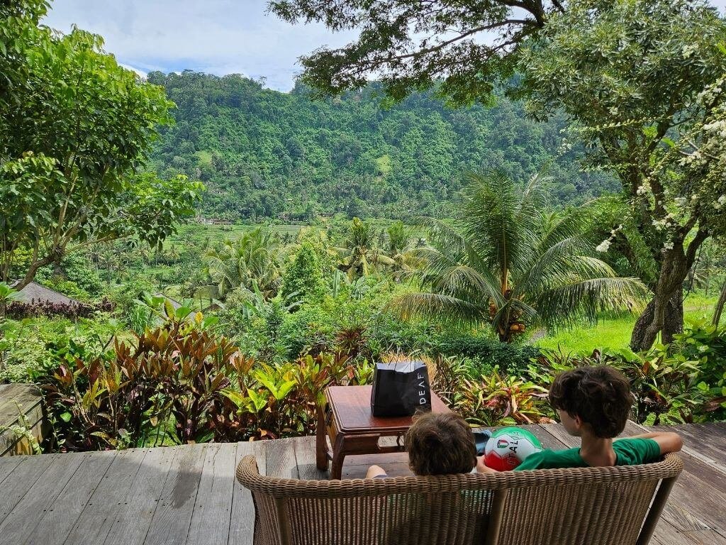 Kinderen zitten samen op een bankje in Sidemen met uitzicht op de rijstvelden tijdens de regen op Bali met kinderen