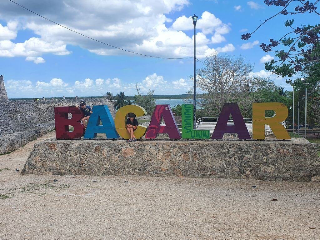 Kinderen poseren bij de kleurrijke Letras Turísticas in Bacalar tijdens een vakantie in Mexico met kinderen