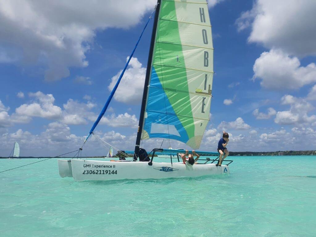 Kinderen springen van een catamaran in het turquoise water van het zevenkleurenmeer van Bacalar tijdens een gezinsvakantie in Mexico met kinderen
